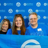 Two alumni and one student pose for a photo with the GV flag
